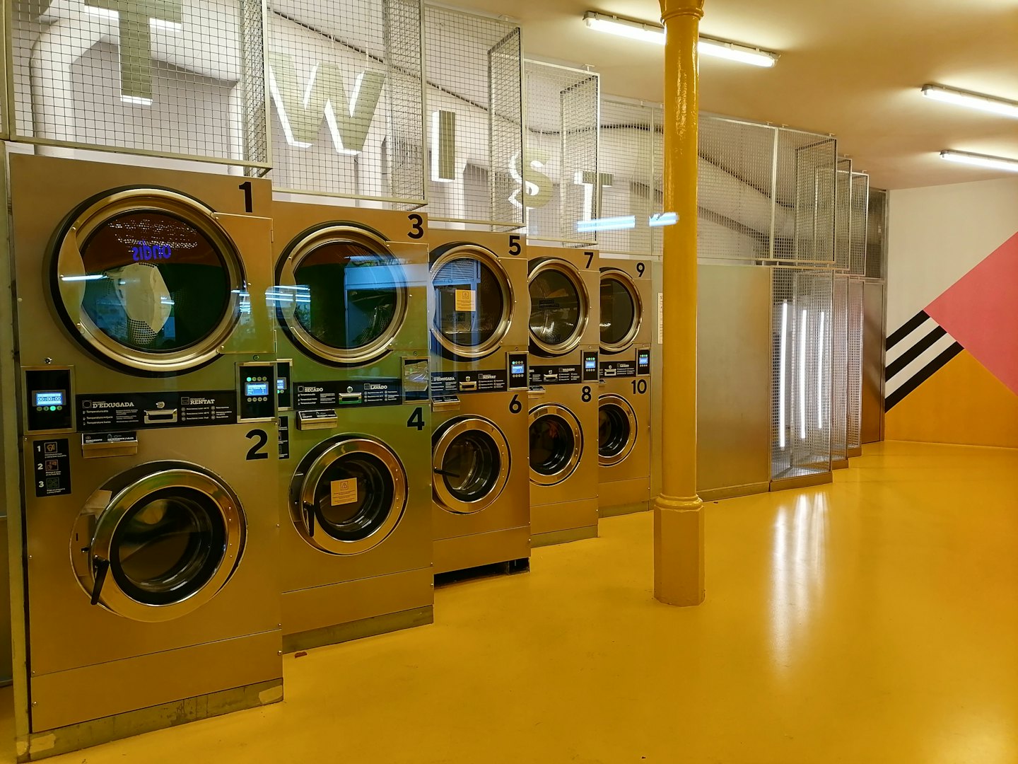 Lavanderia moderna con lavatrici in acciaio inox e pavimento giallo.